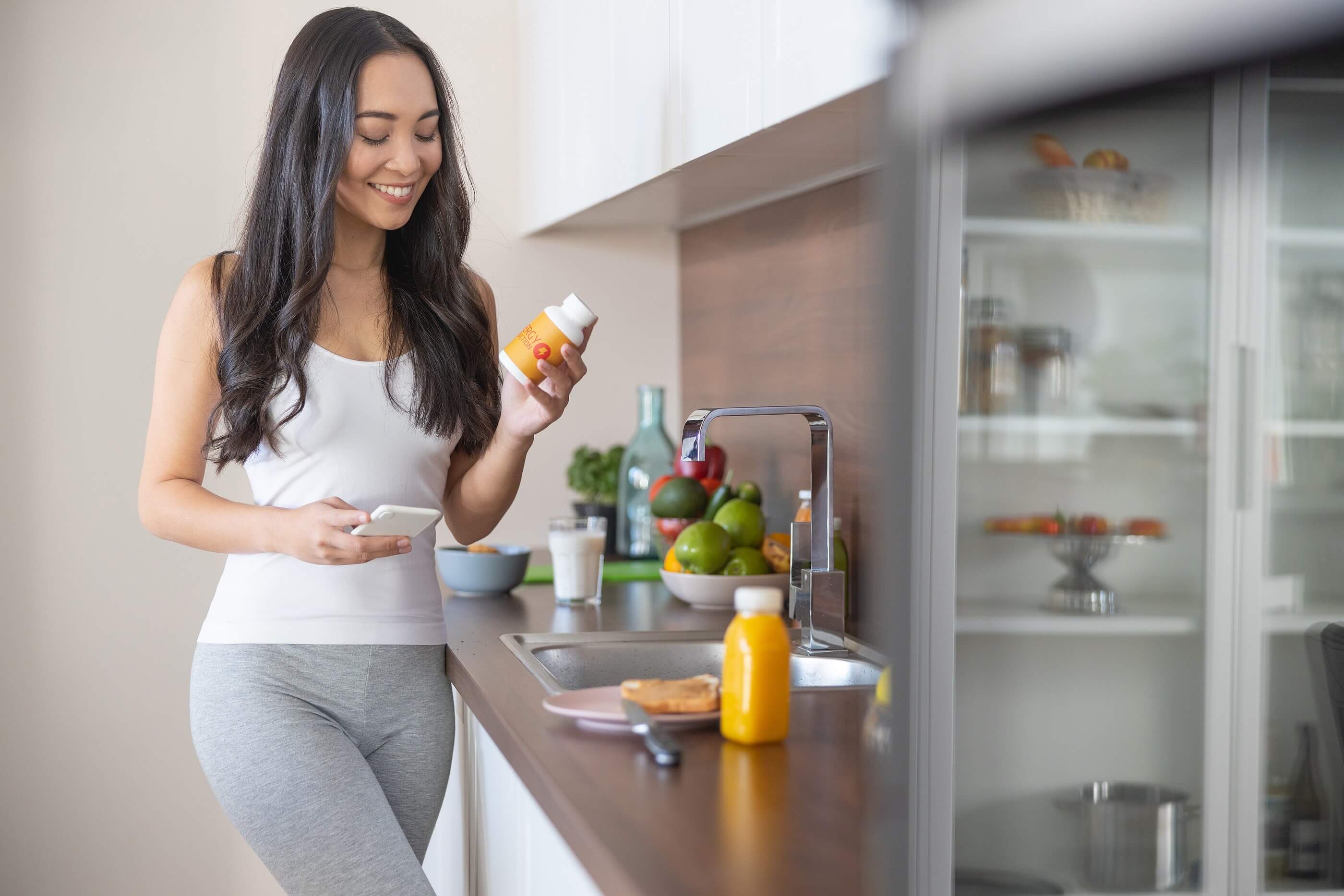 Woman looking at supplement bottle in kitchen