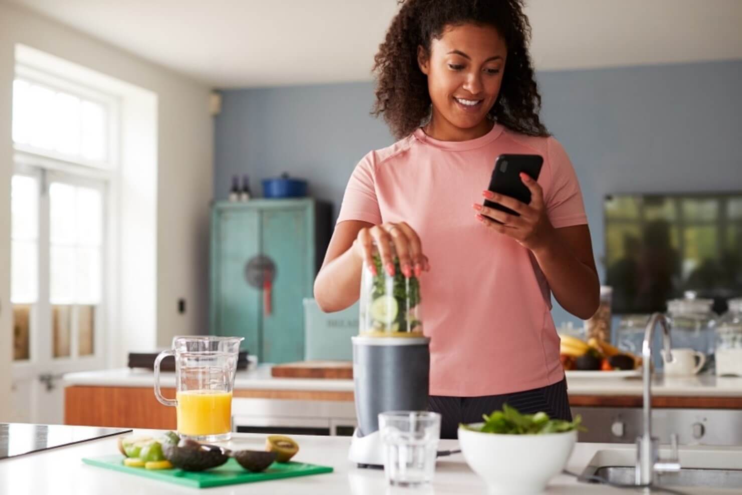 woman looking at phone while making smoothie