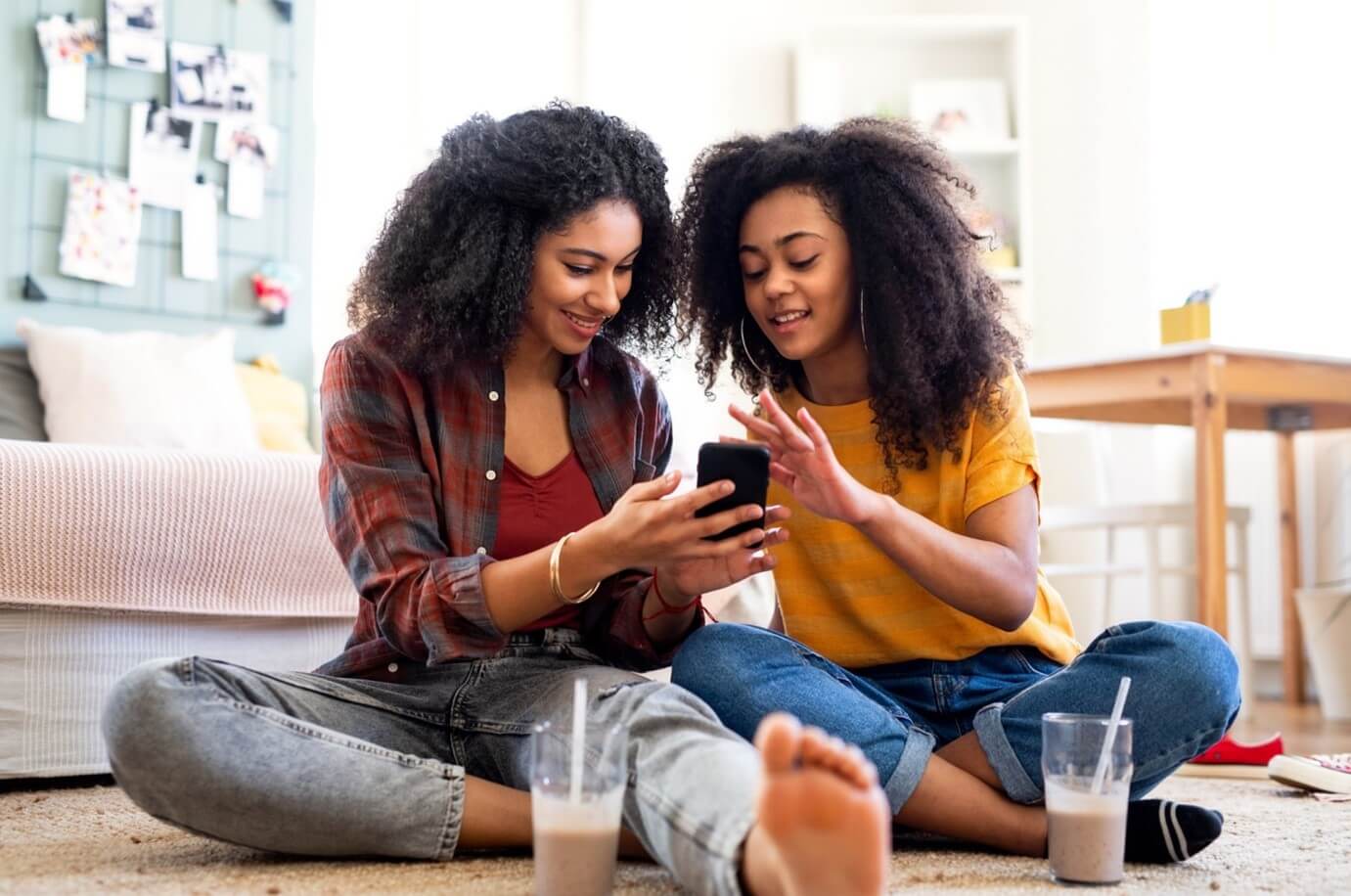 two women looking at phone drinking beverage