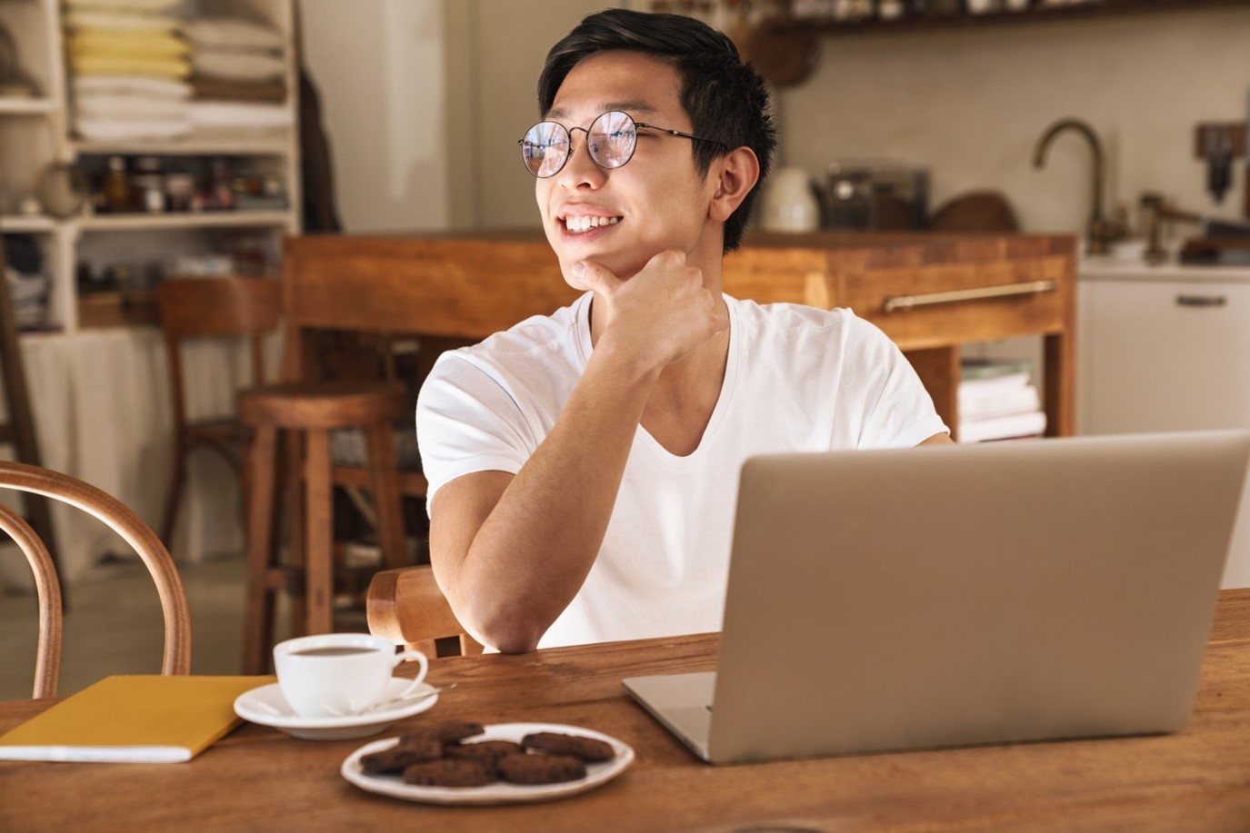 Asian man at computer with snack and coffee