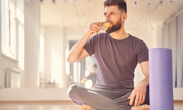 man drinking beverage on yoga mat