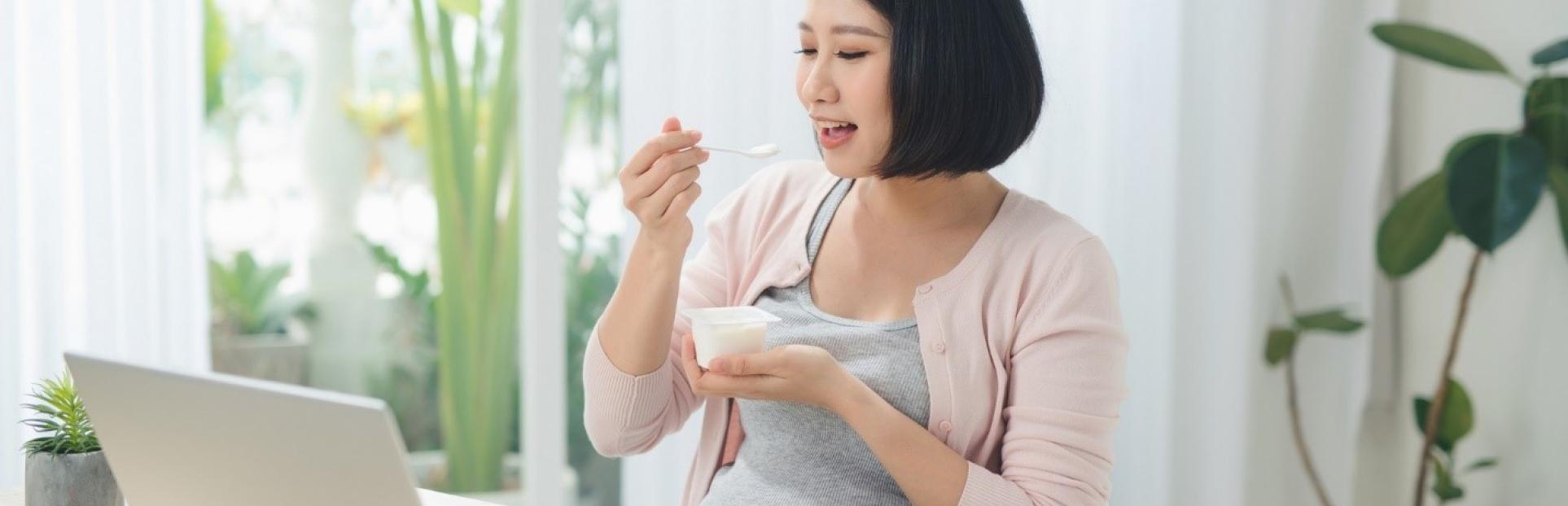 woman eating yogurt at desk with laptop