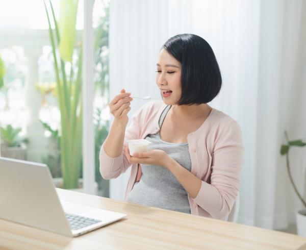 woman eating yogurt at desk with laptop