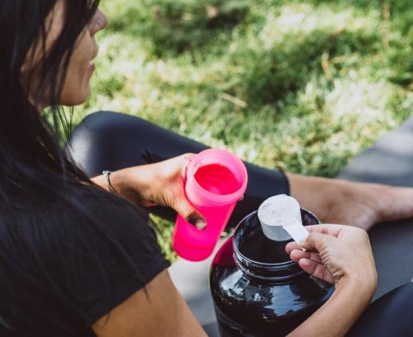 Woman pouring protein powder in drink